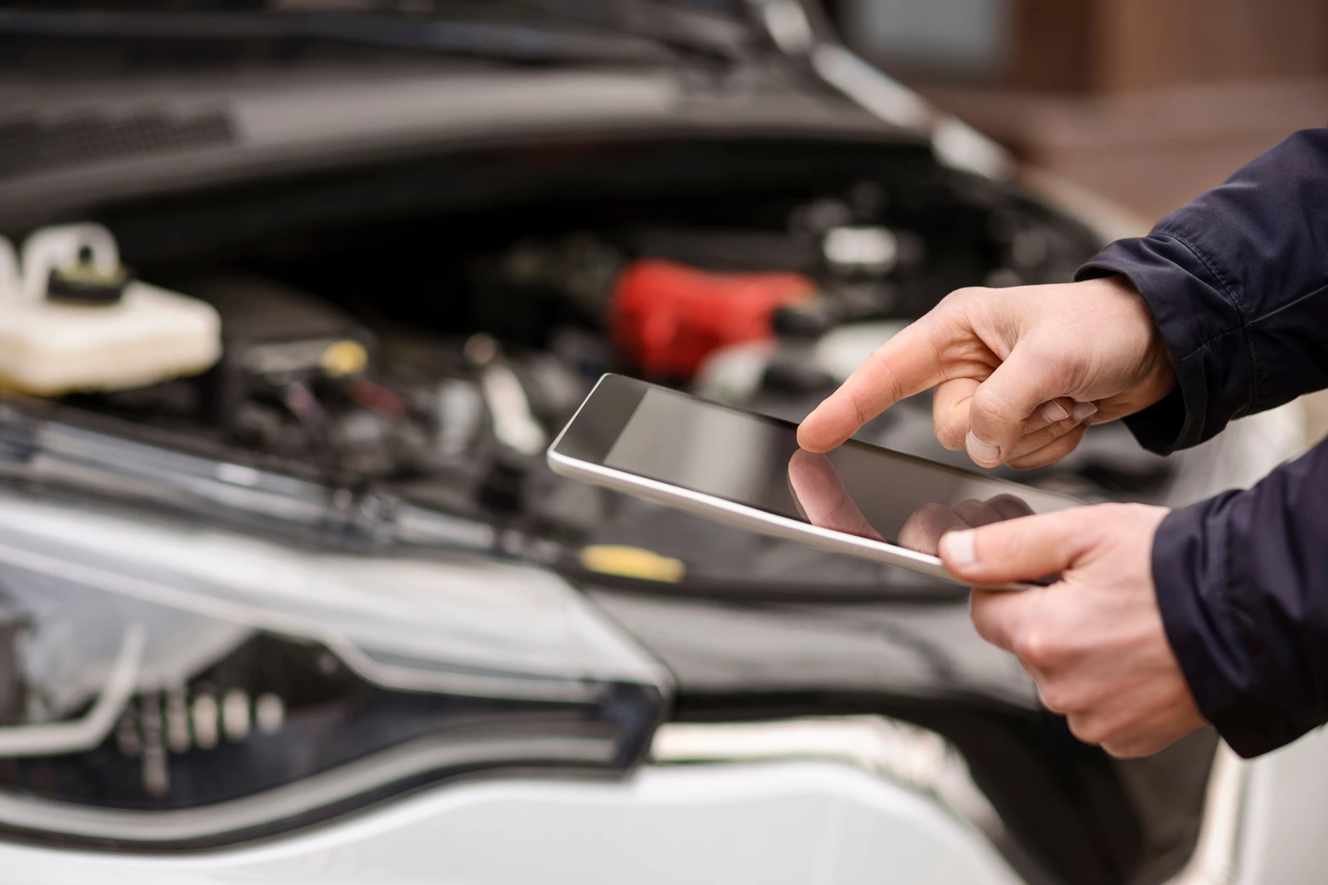 Gros plan professionnel d'un technicien automobile utilisant un équipement de diagnostic électronique connecté à un véhicule dans un atelier automobile moderne. Le technicien porte une tenue professionnelle (chemise ou combinaison) et consulte l'écran de diagnostic affichant des données techniques. L'arrière-plan montre un atelier bien équipé avec le véhicule soulevé ou en position de diagnostic, éclairage professionnel clair. L'image transmet la confiance, l'expertise technique et la modernité du service.