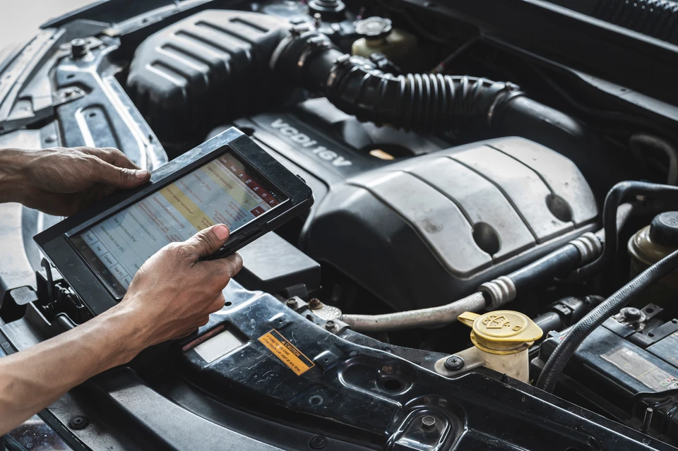 Intérieur véhicule automobile, technicien en combinaison bleue utilise tablette diagnostique connectée par câbles au système électronique